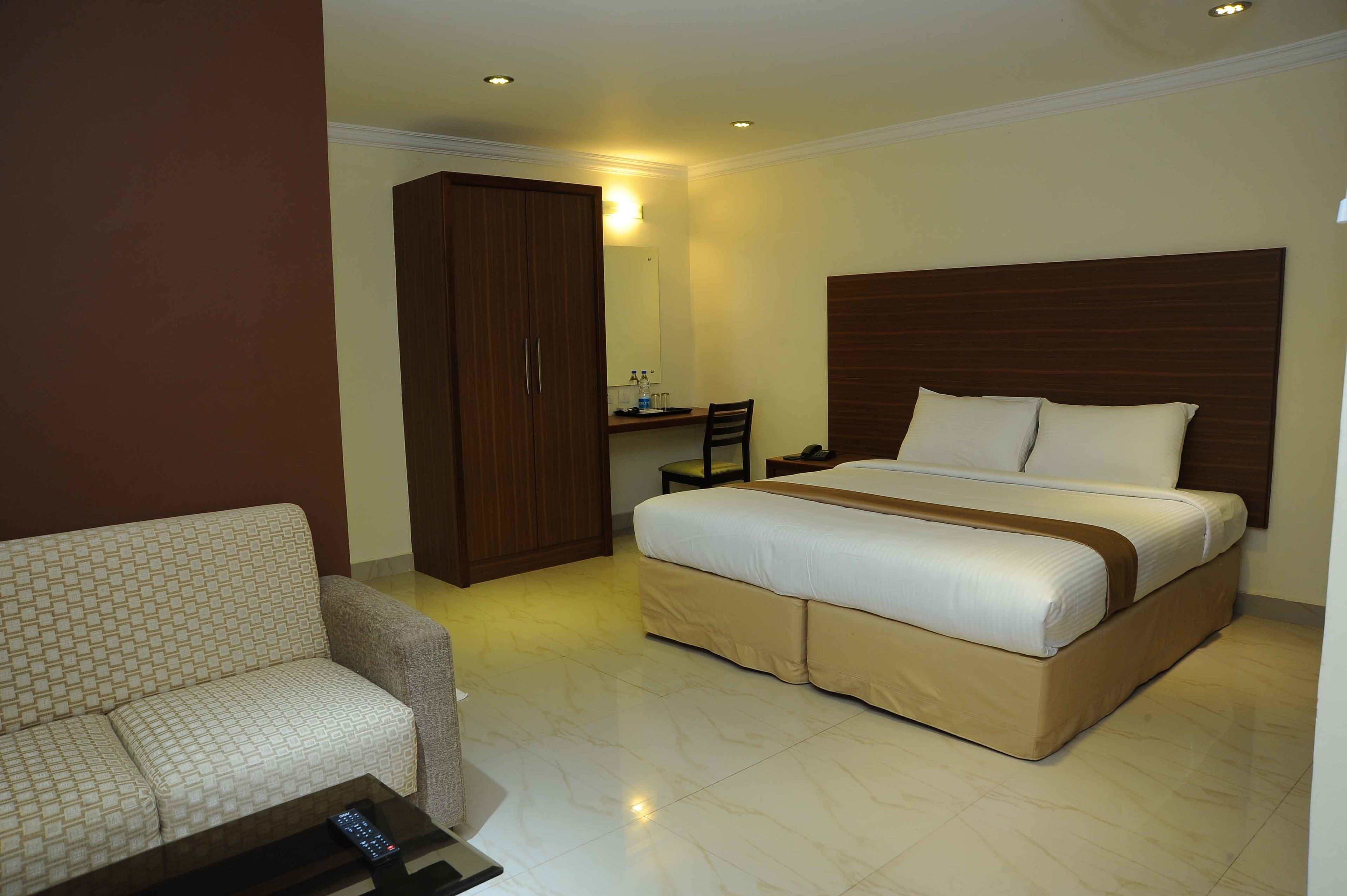 A hotel room with a bed, a sofa, a wardrobe, a desk, and a mirror.