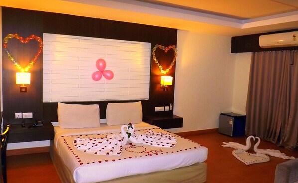 A hotel room with a large bed, two bedside tables, a wall-mounted TV, and decorative wall lights. - Castle International Premium Hotel (Somvarpet)