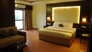 A hotel room with a large bed, a sofa, a desk, and a window with curtains. - Castle International Premium Hotel (Somvarpet)