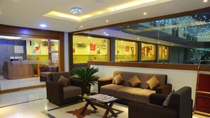 A hotel lobby with a reception desk, seating area with sofas and armchairs, a coffee table, and a large window with decorative lights. - Castle International Premium Hotel (Somvarpet)