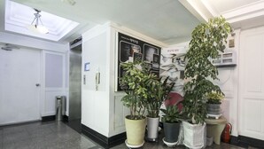 A hotel lobby with a reception desk, a wall-mounted information board, and several potted plants. - Thema Motel (Busan)