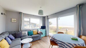 A modern living room with a grey sofa, a small round table, and a striped tablecloth-covered dining table. - B32 Swiss Chalet, Riviere Towans (Hayle)