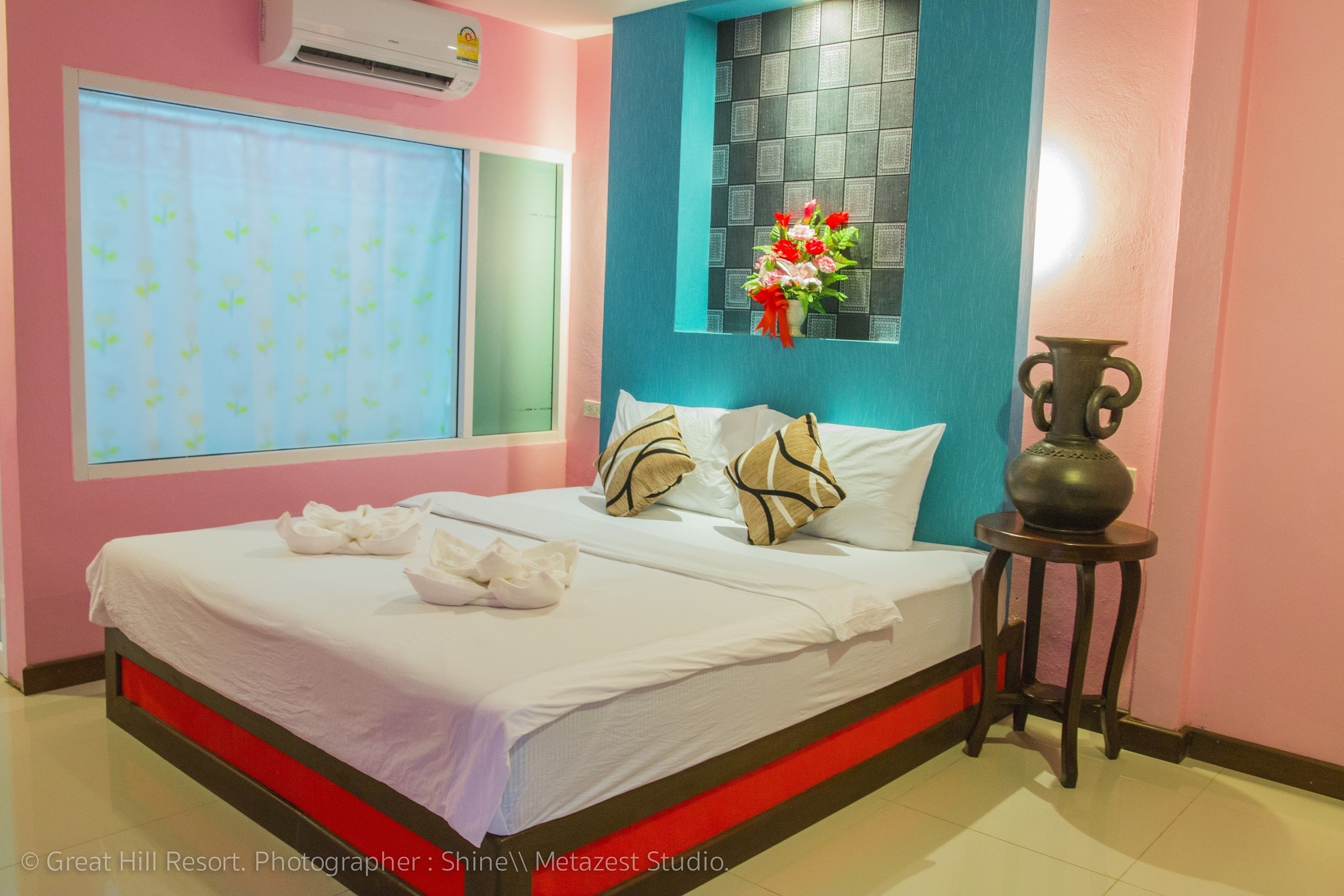 A hotel room with a bed, a window with blinds, a vase with flowers, and a small table.