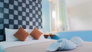 A hotel room with a checkered headboard, a bed with white and brown pillows, a bedside table with a lamp, and a window with a view of the outside.