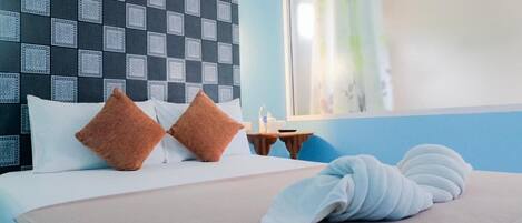 A hotel room with a checkered headboard, a bed with white and brown pillows, a bedside table with a lamp, and a window with a view of the outside.