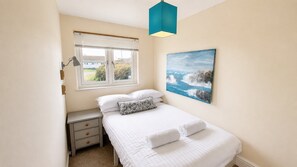 A bedroom with a bed, a nightstand, a window with blinds, a painting, and a blue pendant light.