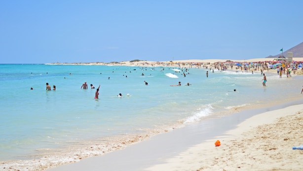Ein Strand mit klarem, blauem Wasser, Sandstrand und Sonnenschirmen.