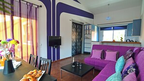 Ein Wohnzimmer mit einem violetten Sofa, einem Couchtisch und einem Essbereich, der für eine Mahlzeit gedeckt ist.