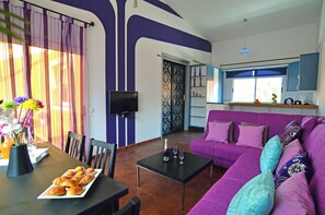A living room with a purple sofa, a coffee table, and a dining area with a table set for a meal.