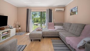 Una sala moderna con un sofá seccional gris, un mueble blanco para el entretenimiento y un televisor grande.