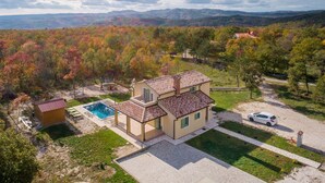Una casa de dos pisos con piscina, rodeada de césped cuidado y árboles.
