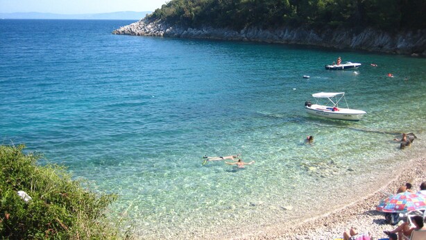 Una playa costera con aguas cristalinas, acantilados rocosos y barcos.