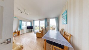 A spacious living area with a dining table, chairs, a television, and a view of the outdoors.
