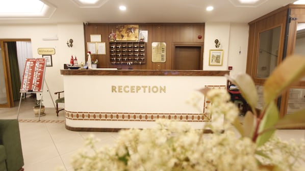 A reception area with a counter labeled "RECEPTION," a menu board, and a wall-mounted wine cooler. - Hotel Ave Maria (Selçuk)