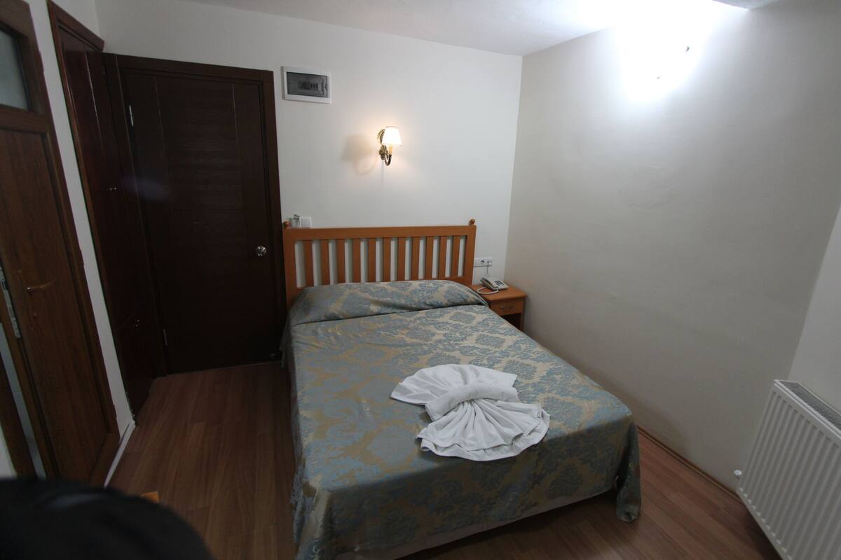A bedroom with a wooden bed, a nightstand, a wall-mounted lamp, and a door.