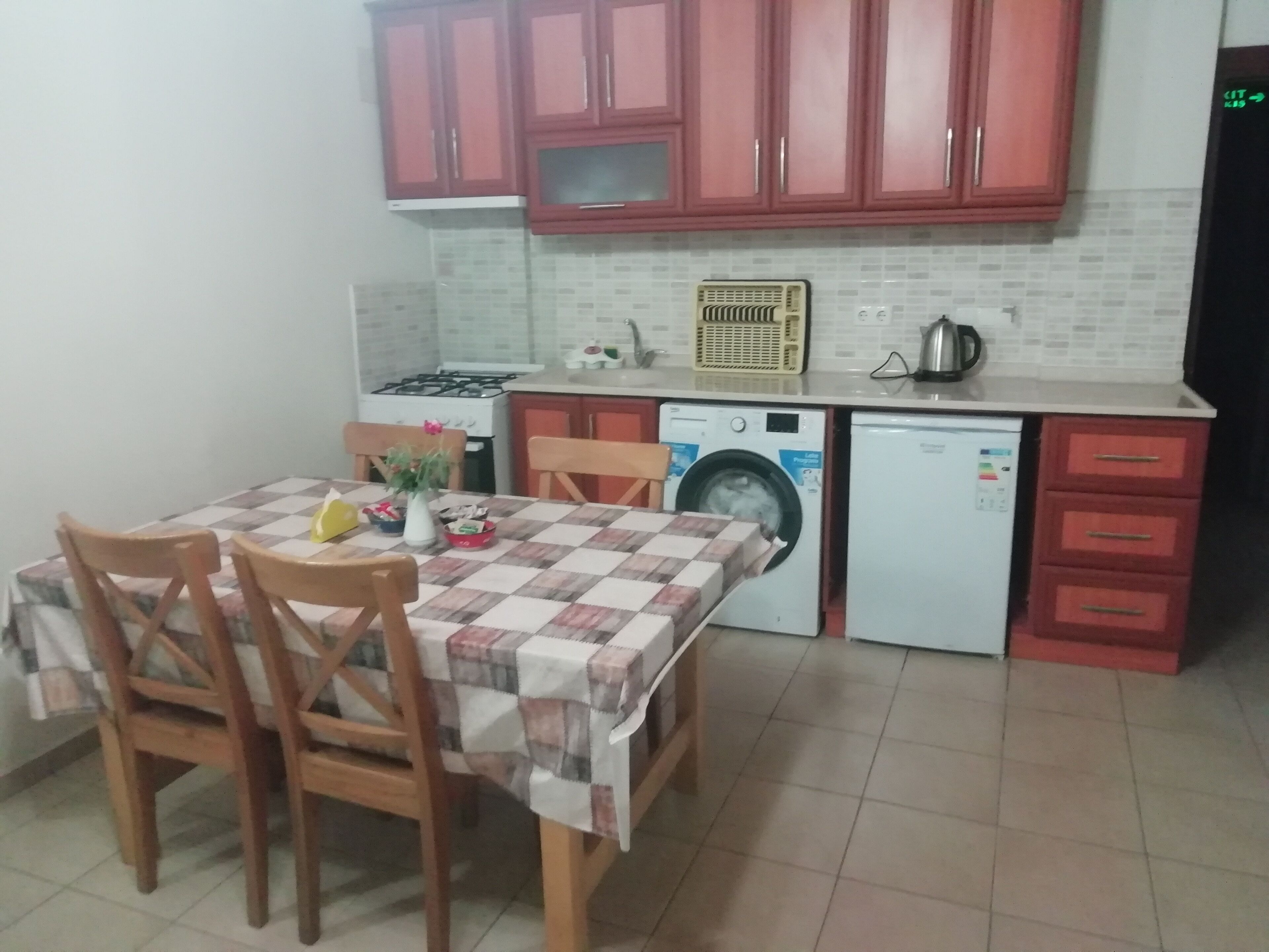 A compact kitchen with a dining table, chairs, a washing machine, a stove, and cabinets.