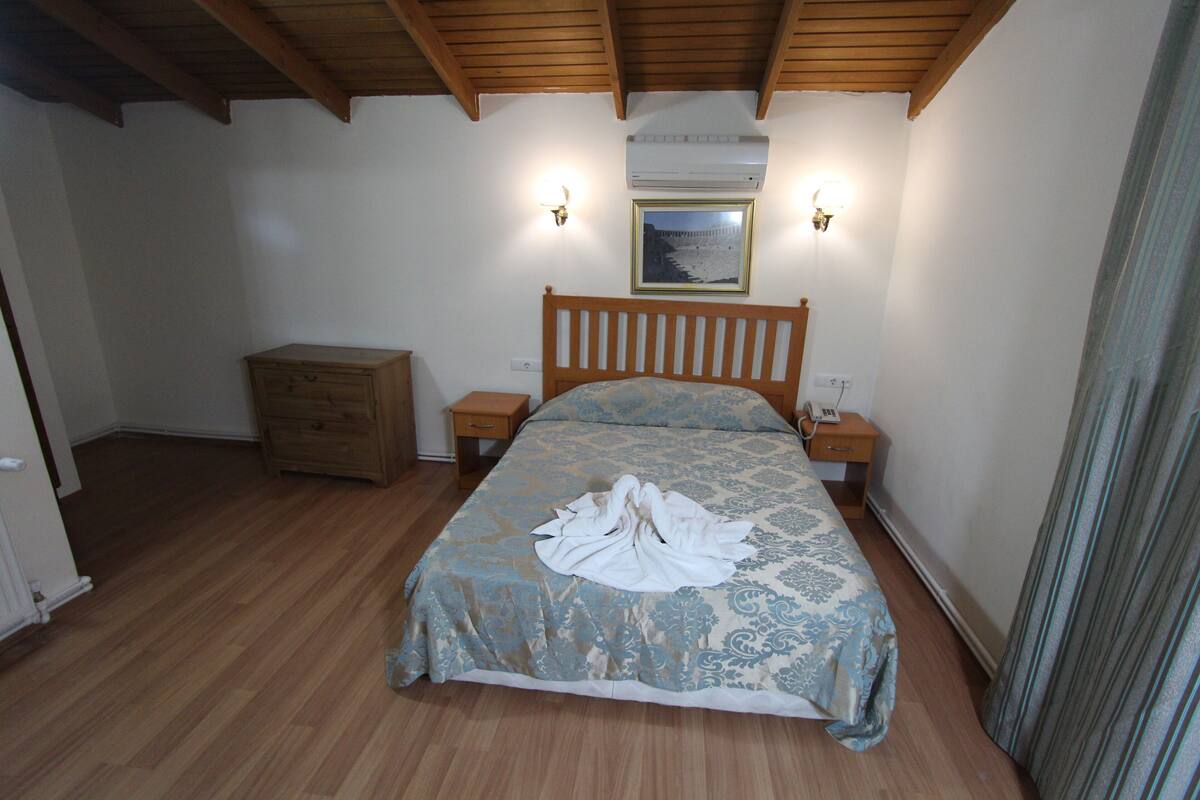 A bedroom with a wooden bed, a nightstand, a dresser, and an air conditioning unit on the wall.