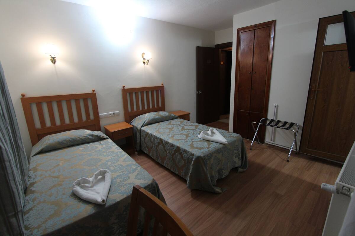 A room with two beds, a wooden wardrobe, a radiator, and a drying rack.