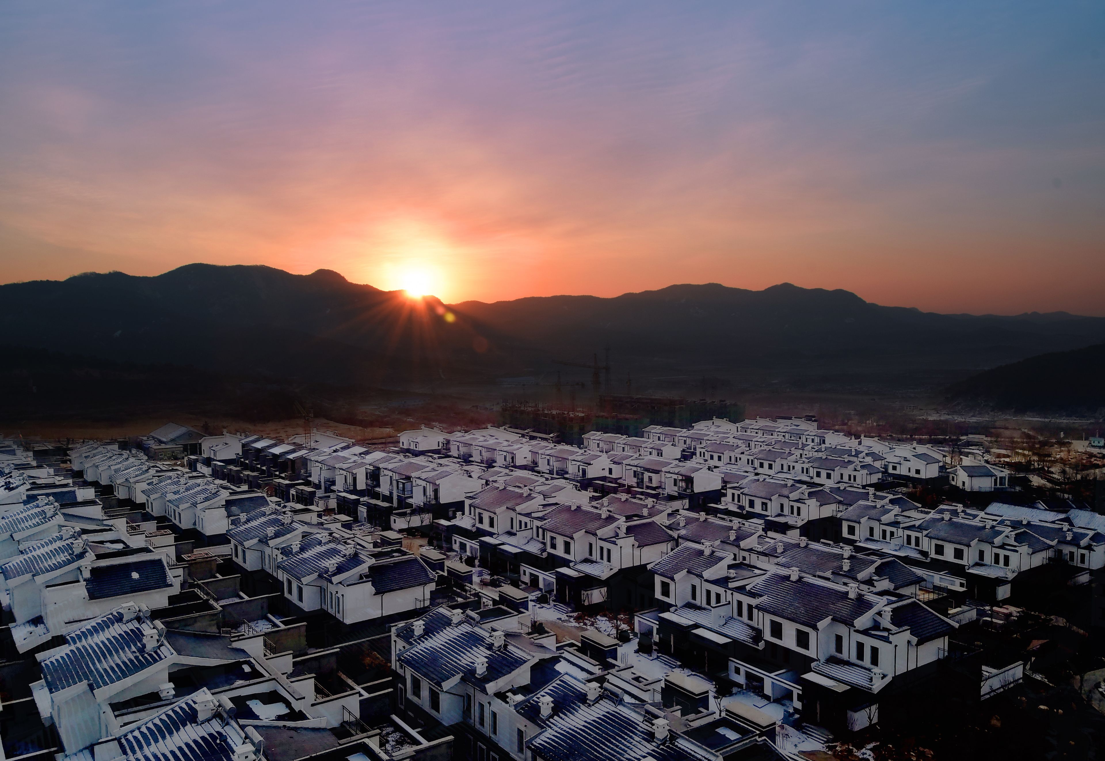 Vista aérea de una zona residencial con casas blancas uniformes y un atardecer al fondo.