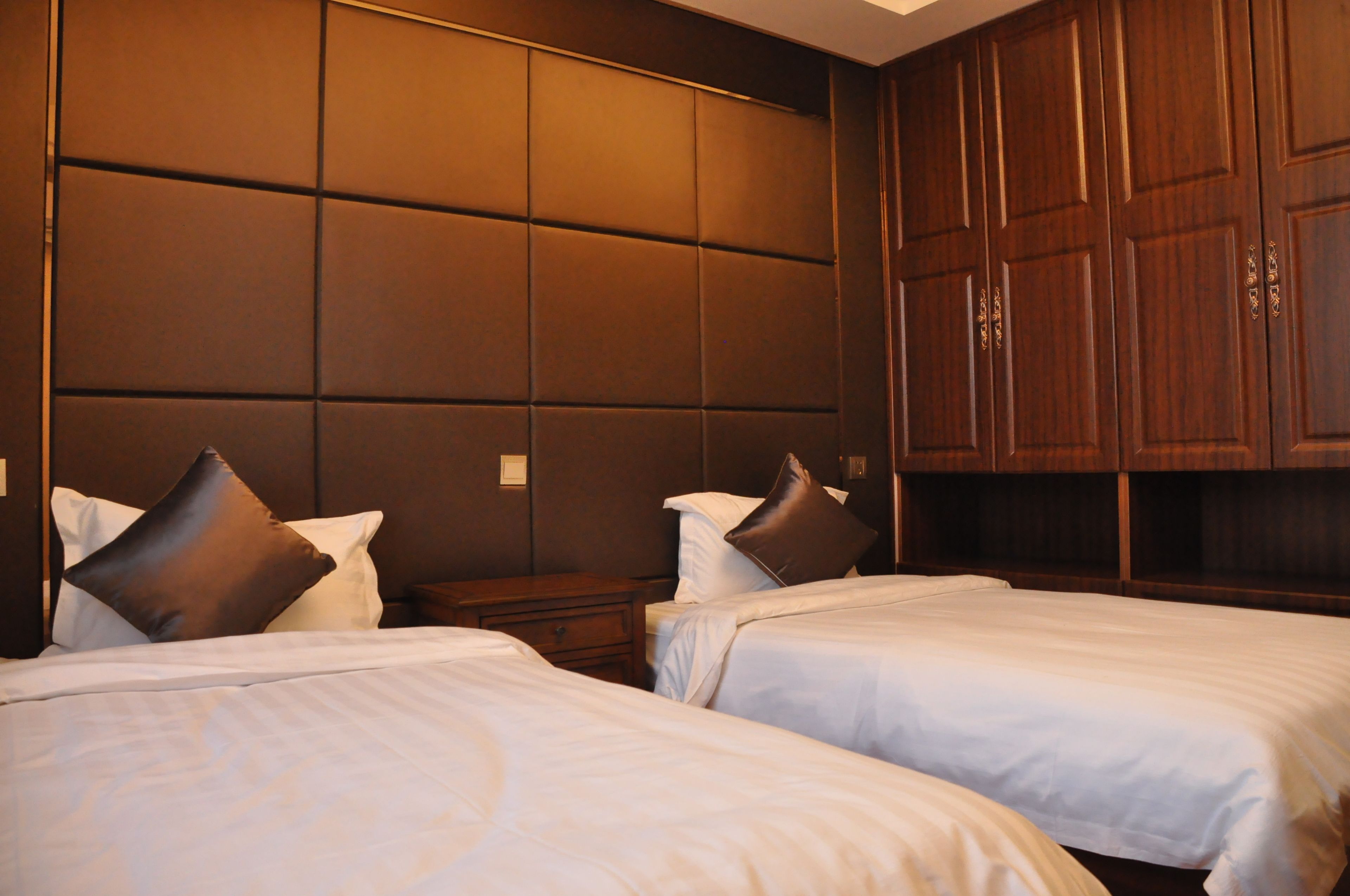 A hotel room with two beds, a large padded headboard, and wooden wardrobe.