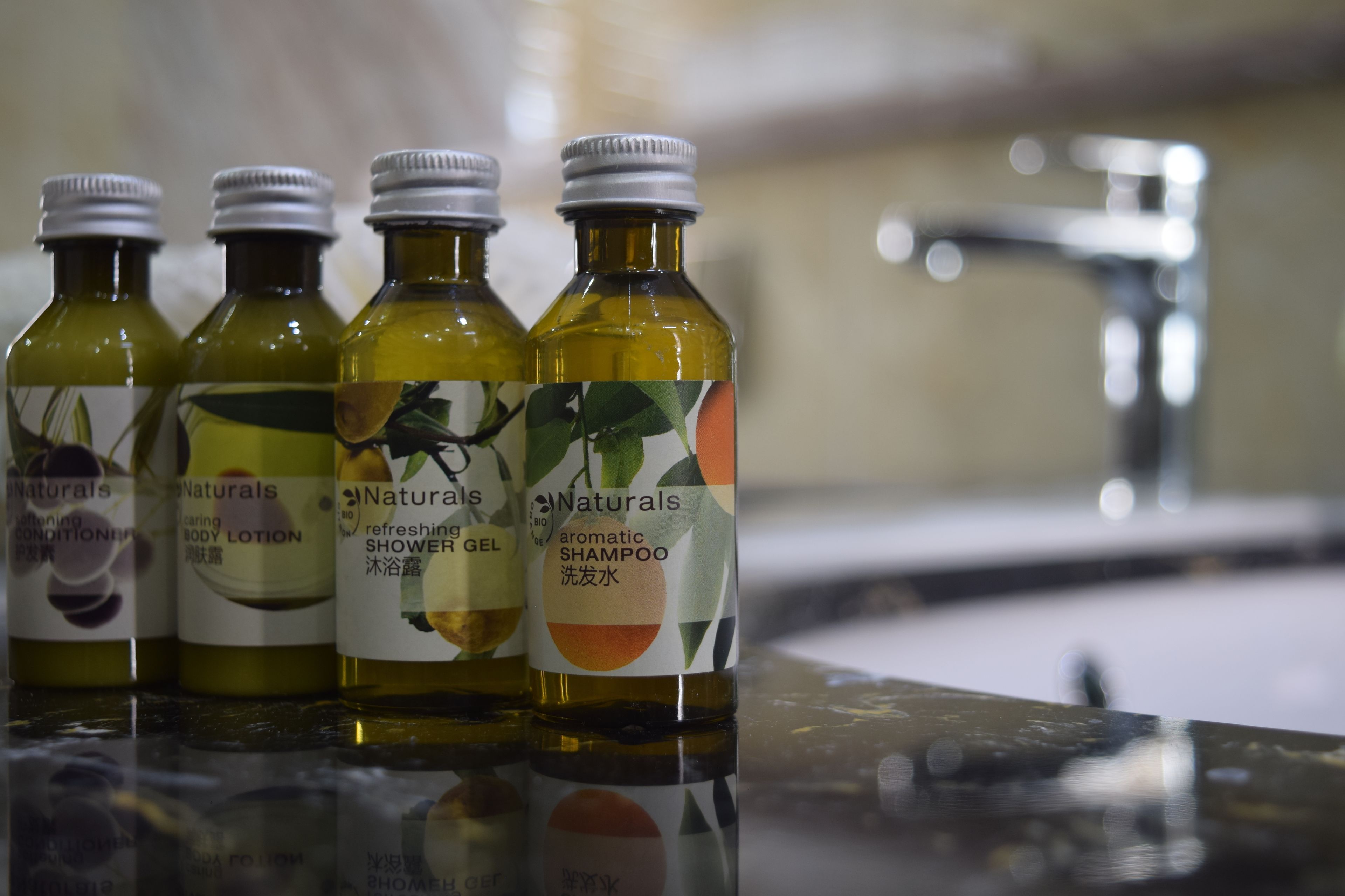 Quatre bouteilles de lotion pour le corps, de gel douche et de shampoing de la marque Naturals, posées sur une surface réfléchissante.