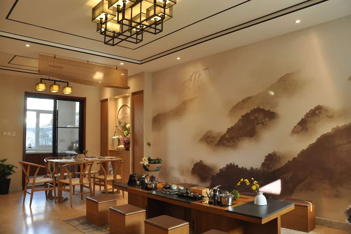Un espace repas avec une table et des chaises en bois, un lustre moderne et une grande fresque murale.