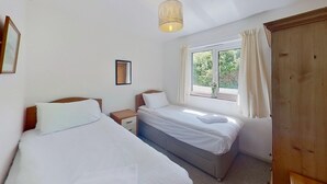Una habitación con dos camas individuales, una mesita de noche, una ventana con cortinas y un armario de madera.