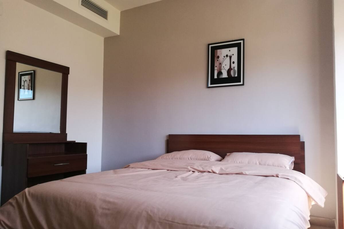 Een slaapkamer met een bed, een dressoir, een spiegel en een lijst met een afbeelding aan de muur.