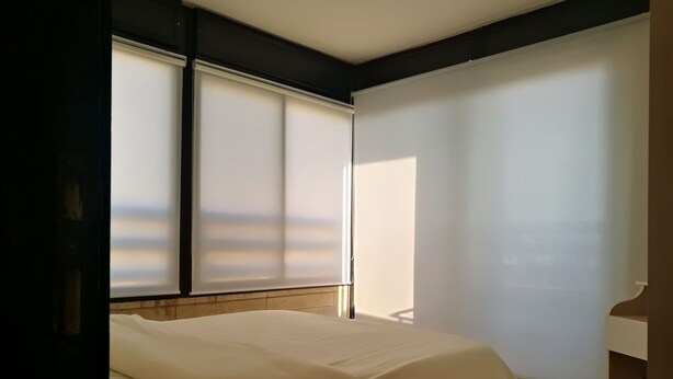 Un dormitorio con cama, ventana con persianas y vista al exterior.