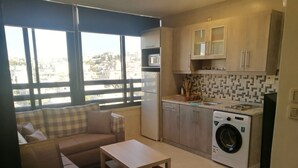 Un espacio habitable compacto con sofá, una mesita, lavadora y zona de cocina con alacenas y salpicadero de azulejos.