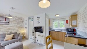 Un espace de vie compact comprenant un canapé, un téléviseur, une cuisine avec des meubles en bois, une fenêtre et un panneau fixé au mur.