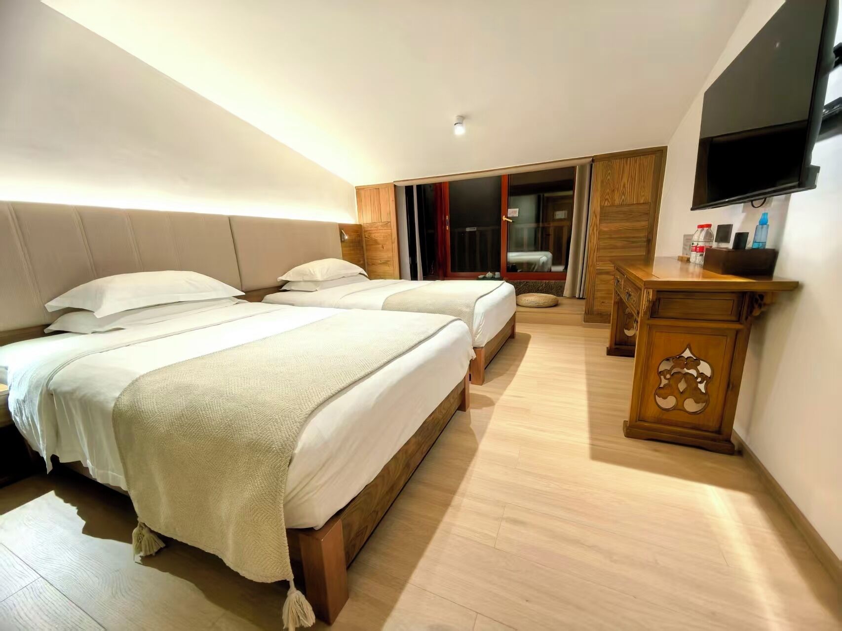 Habitación de hotel con dos camas, una mesita de noche de madera, un televisor de pantalla plana y una puerta corrediza que da a un balcón.