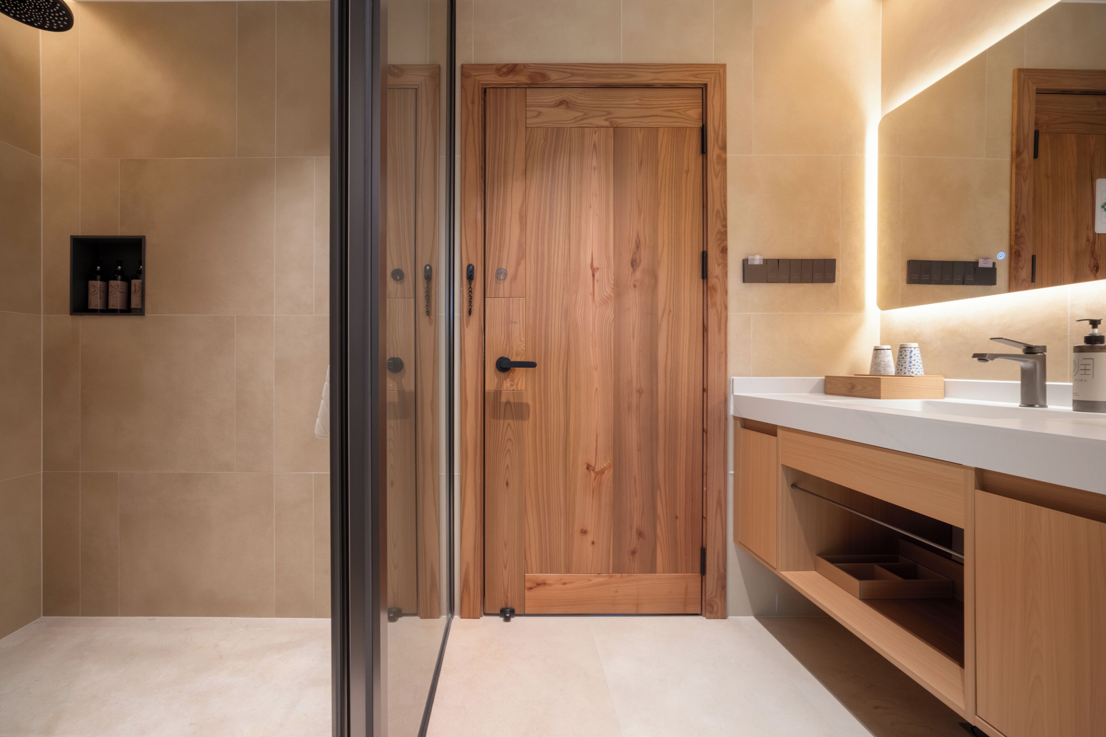 Un baño moderno con puerta de madera, cabina de ducha de vidrio y encimera blanca con espejo.