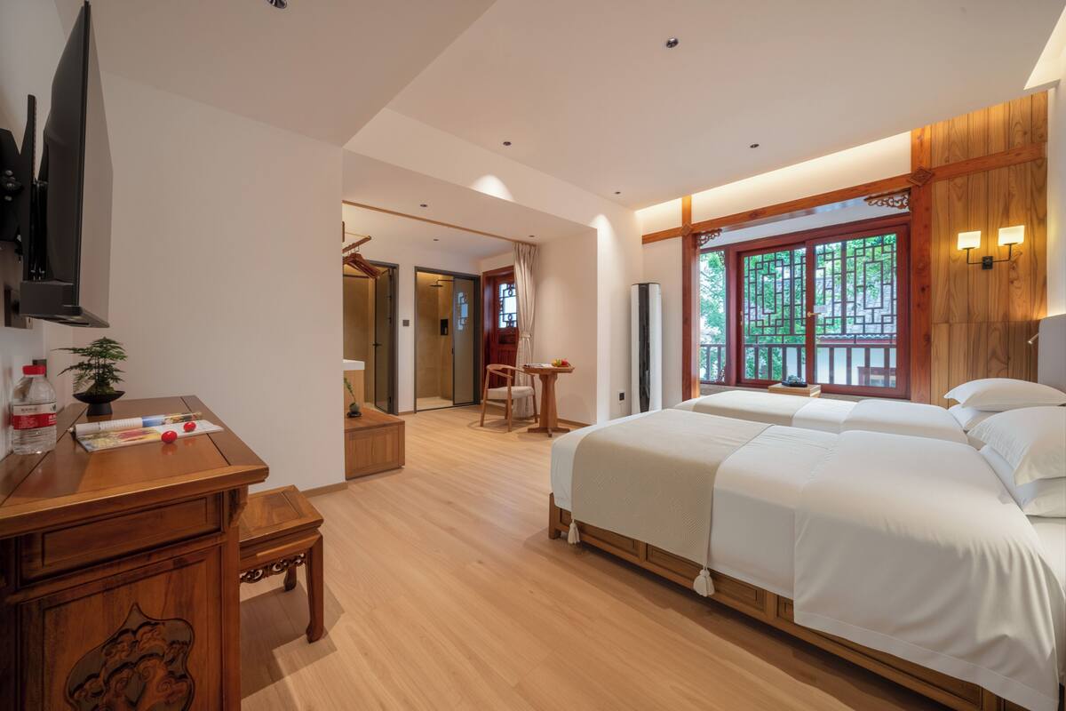A bedroom with a wooden desk, a bed, and a TV mounted on the wall.