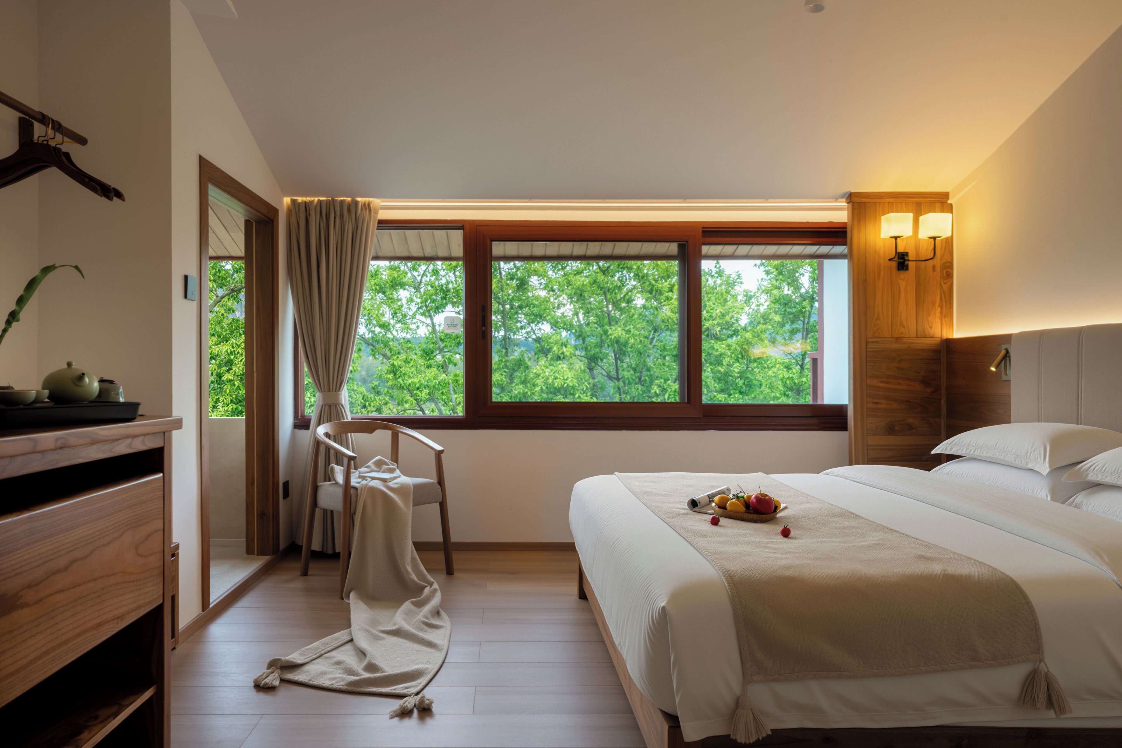 Ein Schlafzimmer mit großem Fenster, einem Bett, einem Sessel, einem Schreibtisch und einem Nachttisch.