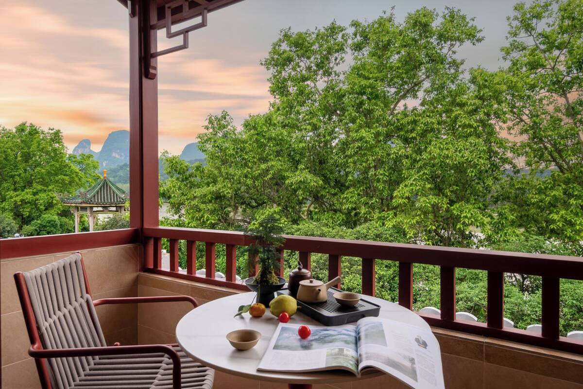 A balcony with a table, chairs, a book, a teapot, and a potted plant.