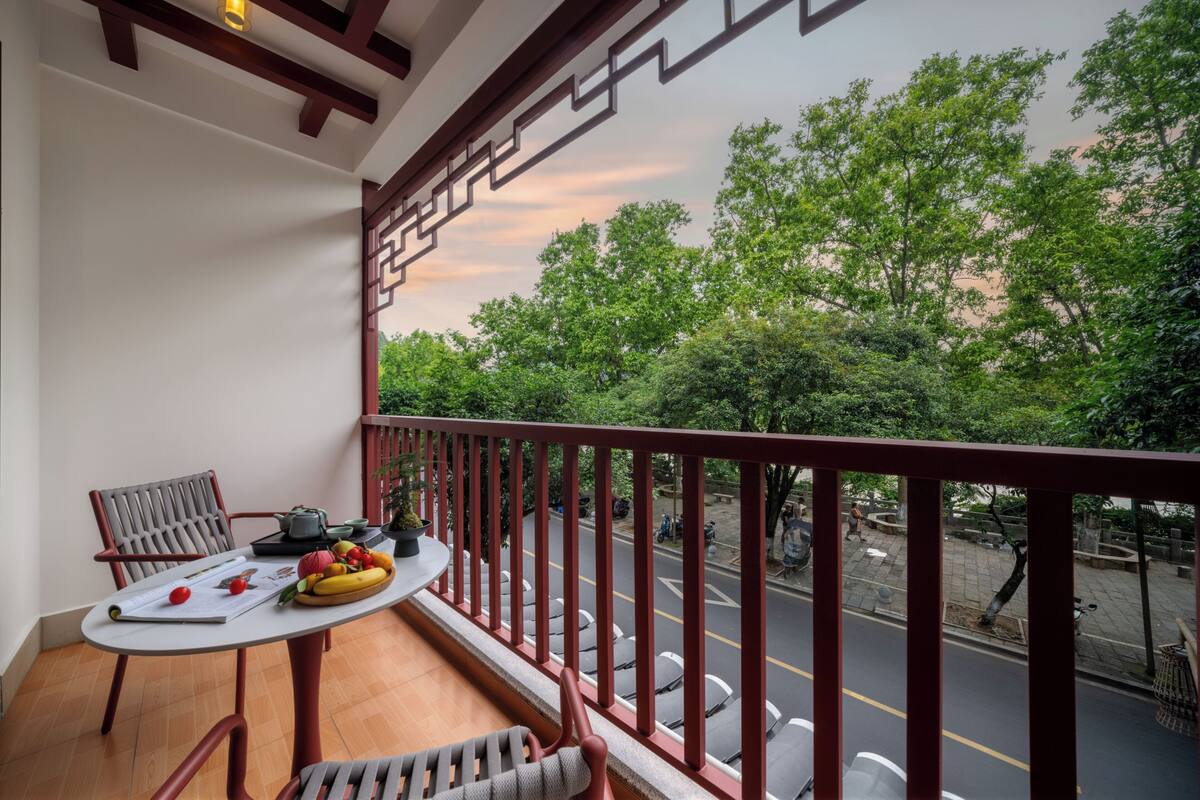 A balcony with a table, chairs, and a view of a street with trees and parked vehicles.