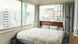 Een hotelkamer met een groot bed, een houten hoofdbord, een raam met gordijnen en uitzicht op de stad.