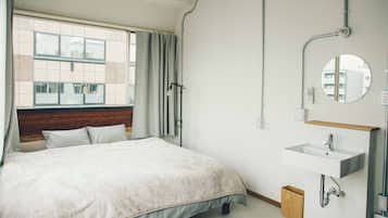 Habitación de hotel con una cama grande, una ventana con cortinas, un baño con lavabo y espejo, y vistas del edificio exterior.