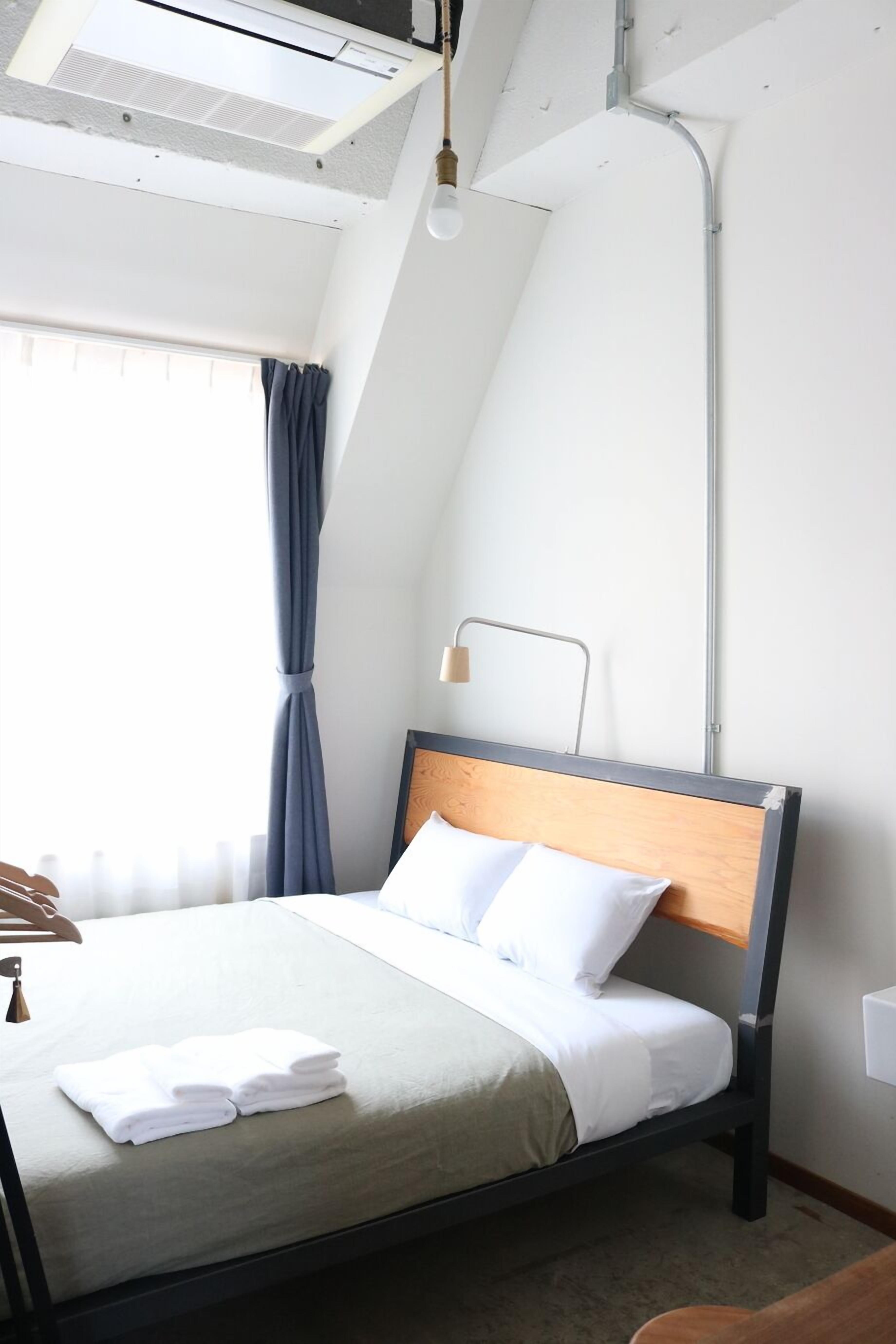A neatly made bed with white linens and a wooden headboard, a bedside lamp, and a window with curtains.