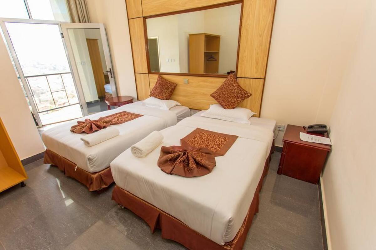A hotel room with two beds, a large mirror, a wooden headboard, and a small desk with a lamp.