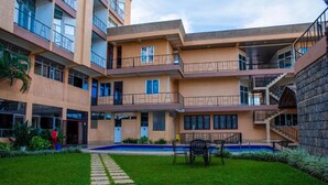 A multi-story building with balconies, a central courtyard with a pool, and a stone wall on one side. - Kigaliview Hotel & Apartaments (Kigali)