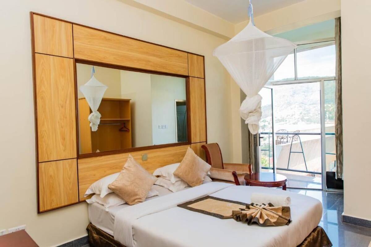 A hotel room with a large bed, a wooden headboard, a large mirror, and a balcony with a view.