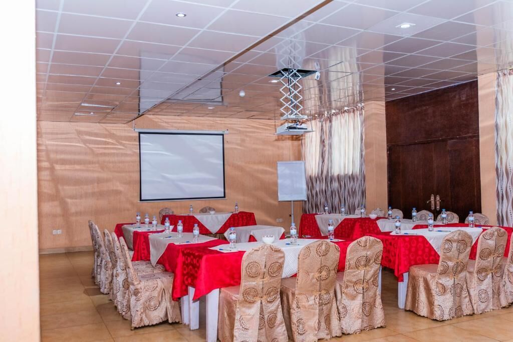 Une salle de conférence dotée de plusieurs tables, chacune recouverte d’une nappe rouge et entourée de chaises blanches aux housses à motifs.