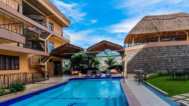 A swimming pool with lounge chairs, a thatched-roof structure, and a stone wall. - Kigaliview Hotel & Apartaments (Kigali)