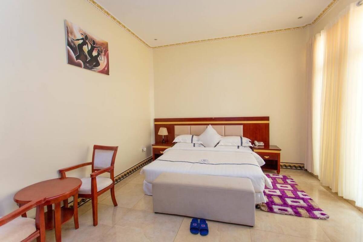 A hotel room with a bed, bedside table, chair, and a small table.