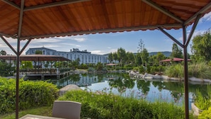 Ein überdachter Außenbereich mit Sitzgelegenheiten und Blick auf ein großes Gebäude sowie einen Teich.