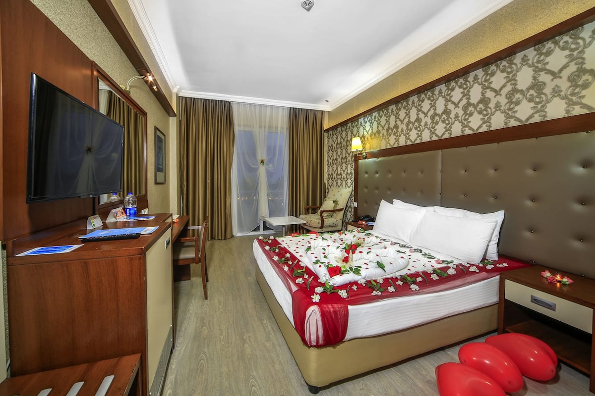 A hotel room with a large bed, a desk with a flat-screen TV, a chair, and a small table.