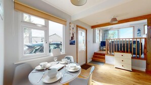 A dining area with a round table set for four, a staircase leading to a loft, and a view of the outside. - C23 Wilmar, Riviere Towans (Hayle)