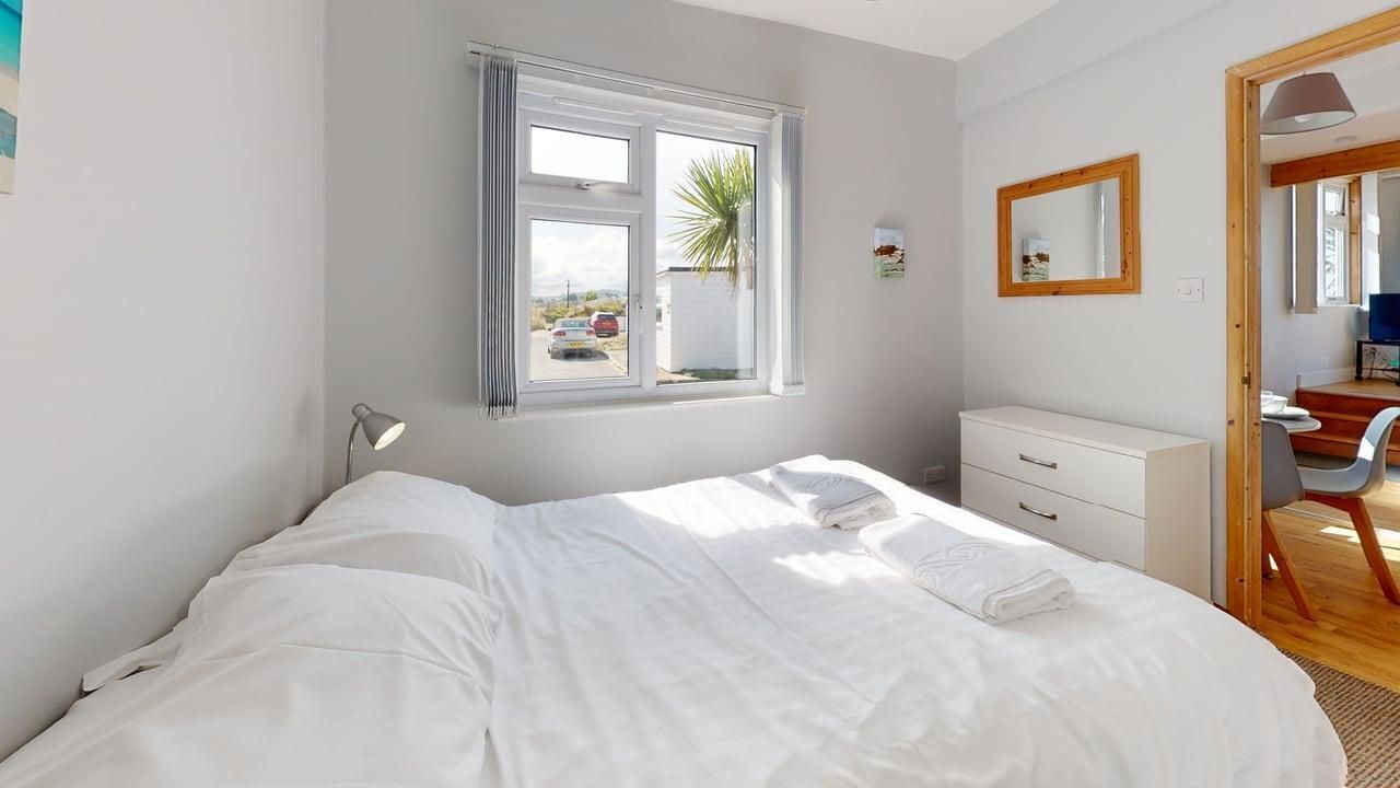 A bedroom with a bed, a desk, a chair, a window, and a mirror.